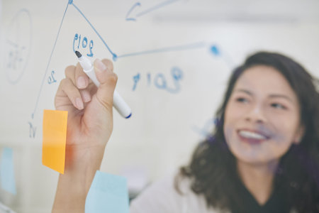 Close-up image of young businesswoman writing financial data on glass wall when getting ready for...