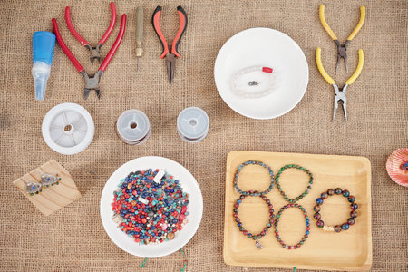 Pliers, wire cutters, beads and tray with handmade gemstone bracelets on tableの写真素材