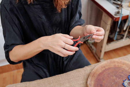 Close-up image of woman using pliers to attach french hook to earring she madeの写真素材
