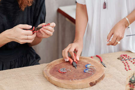 Cropped image of women making earrings with blue and red beadsの写真素材