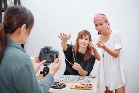Mixed-race young woman talking in front of camera and explaining how to make natural stone necklace at homeの写真素材