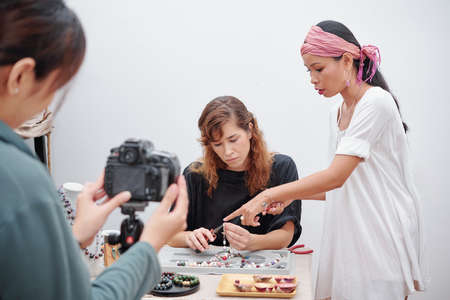 Photographer filming woman making natural stone jewelry under control of teacher at workshopの写真素材