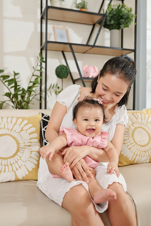 Cute happy little girl sitting on laps of her mother and looking at camera