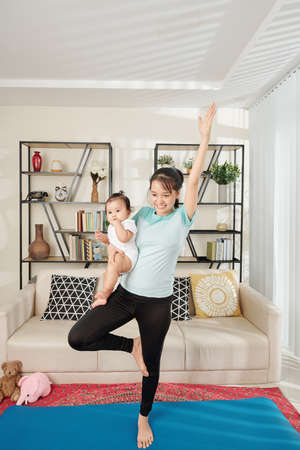 Young Vietnamese woman carrying baby when repeating exercise after fitness training she is watching onlineの写真素材