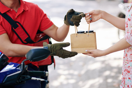 Hands of courier giving order of natural organic yogurt to female client