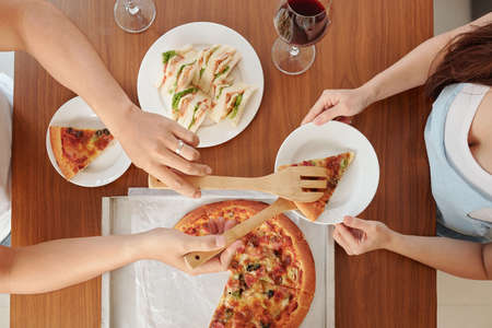 Husband putting slice of homemade pizza in plate of his wife, view from aboveの写真素材
