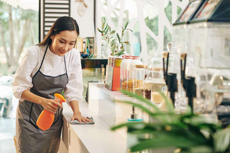 Smiling young cafe worker wiping surfaces with disinfecting detergentの写真素材