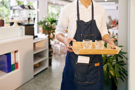 Cropped image of waiter carrying wooden tray with glasses of fresh cold waterの写真素材