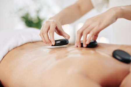 Close-up image of masseuse putting warm basalt stones along spine of client