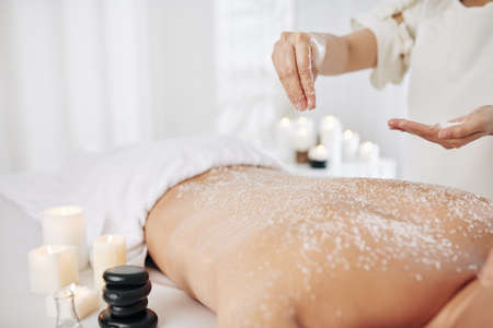 Beautician applying salt scrub on back of male client to get rid of dead skin before massageの写真素材
