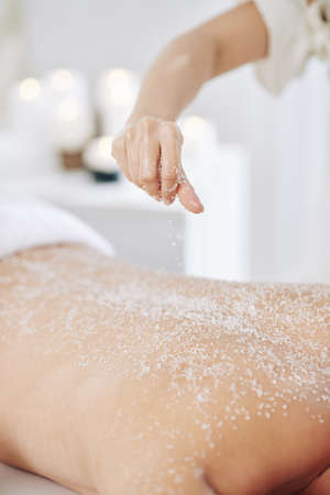 Cosmetologist applying coarse salt peeling on back of clientの写真素材