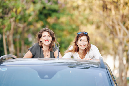 Portrait of beautiful smiling young women standing in car trunk and looking at camera