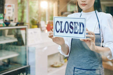 Sad female restaurant owner closing door and hanging signの写真素材