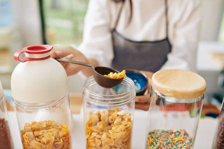 Waiter using plastic spoon when filling bowl with organic cornflakesの写真素材