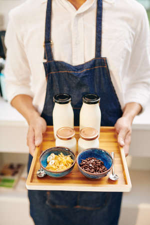 Cropped image of waiter holding tray with breakfast consisting of fresh yogurt, cornflakes and bottle of milkの写真素材