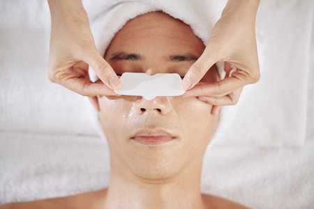 Cosmetologist applying nose strip on nose of young man to clear pores