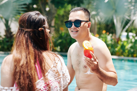 Happy young Asian man spending time in swimming pool with his girlfriend and enjoying delicious...