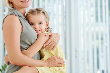 Cute little girl hugging her mother tight and looking at camera