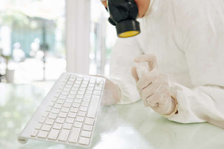 Cleaning service worker in protective mask spraying keyboard with anti-bacterial sprayの写真素材