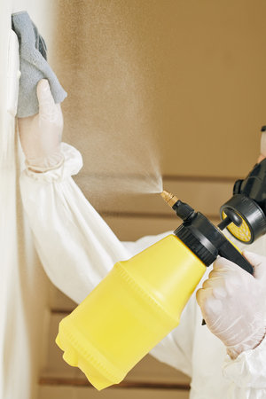 Close-up image of worker in protective suit and rubber gloves cleaning light switch with...