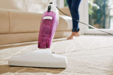 Close-up image of woman vacuum cleaning carpet in main room of her houseの写真素材