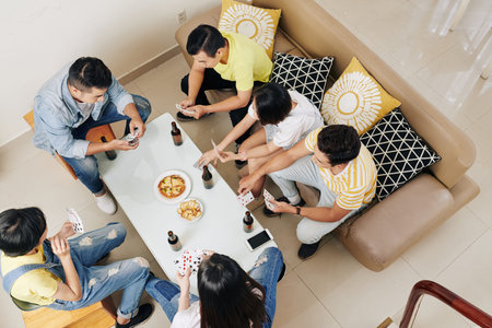 Group of friends gathered at home to have some snacks, drink beer and play cards