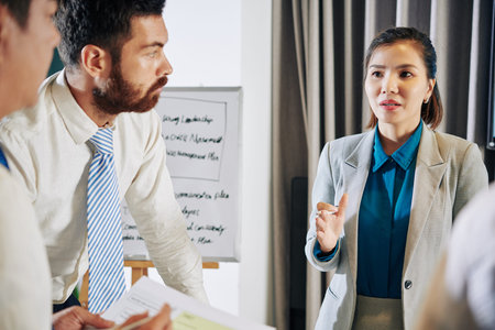 Concerned young businesswoman talking to coworkes and discussing ani-crising measuresの写真素材