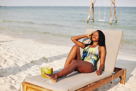 Beautiful young Black woman enjoying sunbathing and drinking refreshing coconut waterの写真素材