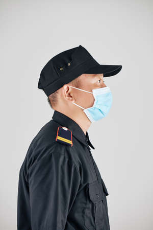Side view of serious police officer in uniform and medical mask, isolated on greyの写真素材