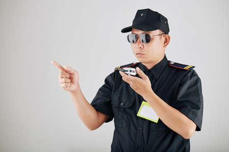 Serious policeman in sunglasses using walkie-talkie or police radio during demonstration and contolling work of officersの写真素材