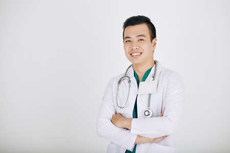 Portrait of hapy smiling young Vietnamese doctor crossing arms and looking at camera, isolated on shiteの写真素材