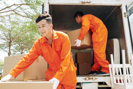 Two young adult men wearing orange uniform clothes loading truck with household things