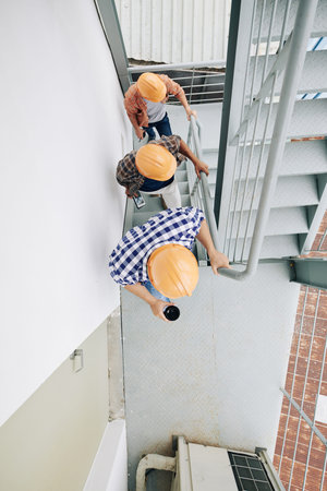 Vertical from above view shot of three unrecognizable construction specialists wearing hardhats...
