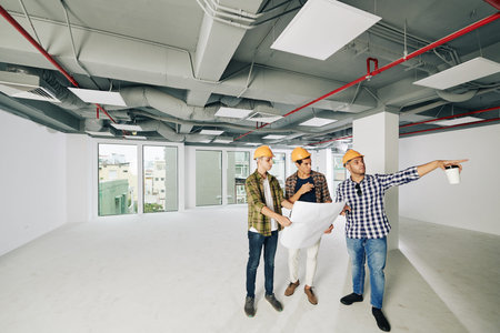 Three professional construction engineers wearing hardhats standing together inside new building...