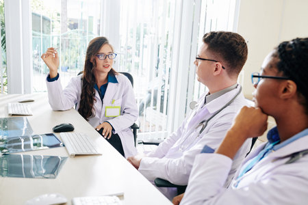 Young female serious pulmonologist talking to colleagues at meeting and discussing latest news on...