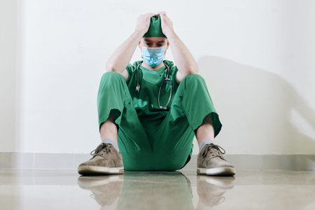 Stressed tired young surgeon sitting on the floor in hospital corridor after difficult surgery