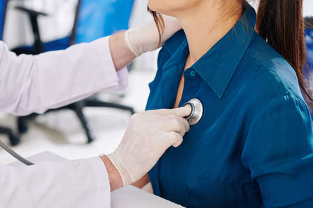 General practitioner in medical gloves listening to young woman breathingの写真素材