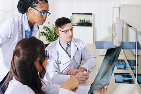 Group of concerned young doctors discussing lungs x-ray of patient with suspected COVID-19の写真素材