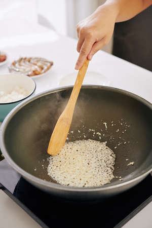 Woman frying diced onion in cooking pan and mixing it with wooden spatulaの写真素材