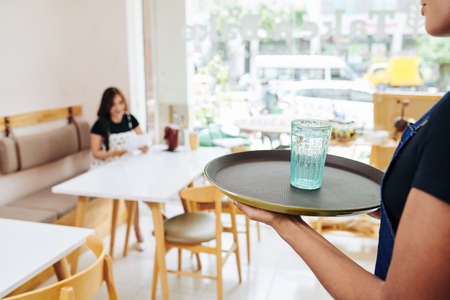 Waiter bringing glass of water to female customer sitting in the corner by windowの写真素材
