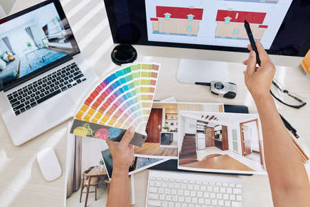 Interior designer working on color scheme for interior and exterior of clients house, he is holsing color palette and pointing at laptop screen with stylusの写真素材
