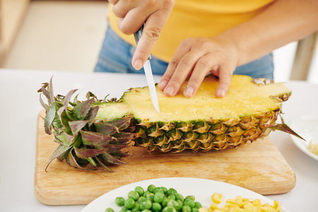 Close-up image of woman cutting fresh ripe pineaaple with sharp ceramic knifeの写真素材