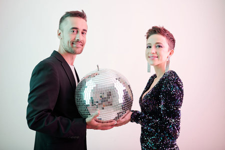 Smiling male and female singers holding disco ball and looking at cameraの写真素材