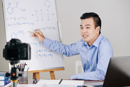 Science teacher drawing chemical formulas on whiteboard when hosting online lesson for college studentsの写真素材