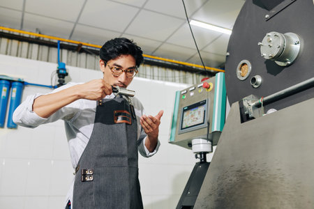 Barista standing at roasting machine and smelling coffee beans in probe to check if they are ready