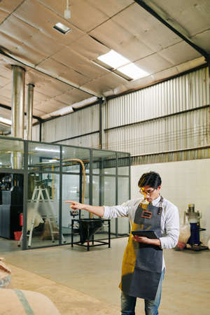 Roastery owner reading list on tablet computer when checking sacks with roasted coffee in storageの写真素材