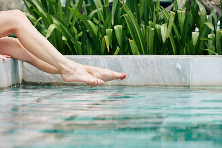 Beautiful legs of young woman splashing water in swimming poolの写真素材