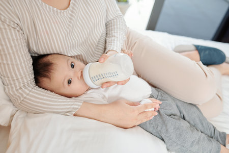 Mother lying in bed and feeding her little daughter with formula in a bottle