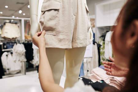Young female customer touching fabric of beige shorts on mannequin in shopping mallの写真素材