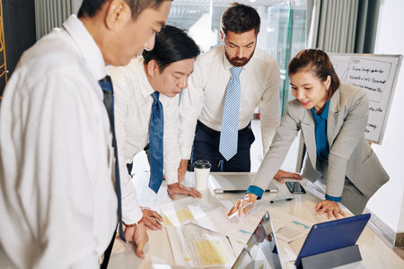 Positive female entrepreneur showing charts and diagrams to colleagues when discussing strategy of...